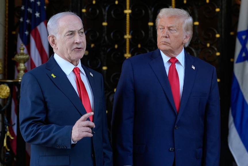 Benjamin Natanyahu and Donald Trump stand side-by-side in front of US and Israeli flags. They are bother wearing suits. 