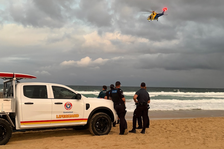 LIfeguards beside ute as helicopter flies overhead over water