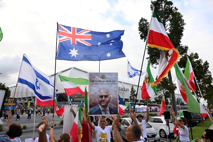 Iranian, Australian and Israeli flags fly as demonstrators hold up a sign praising Reza Pahlavi.