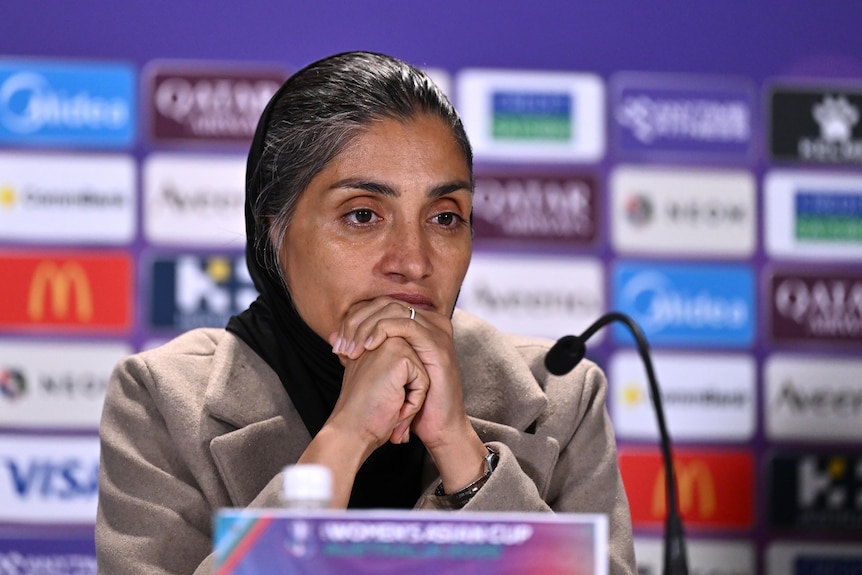 Iran's women's football team coach Marziyeh Jafari has her hands on her chin as she fronts a press conference