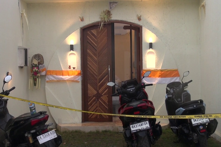 Three scooters parked behind police tape cordoning off an open entry to a villa.