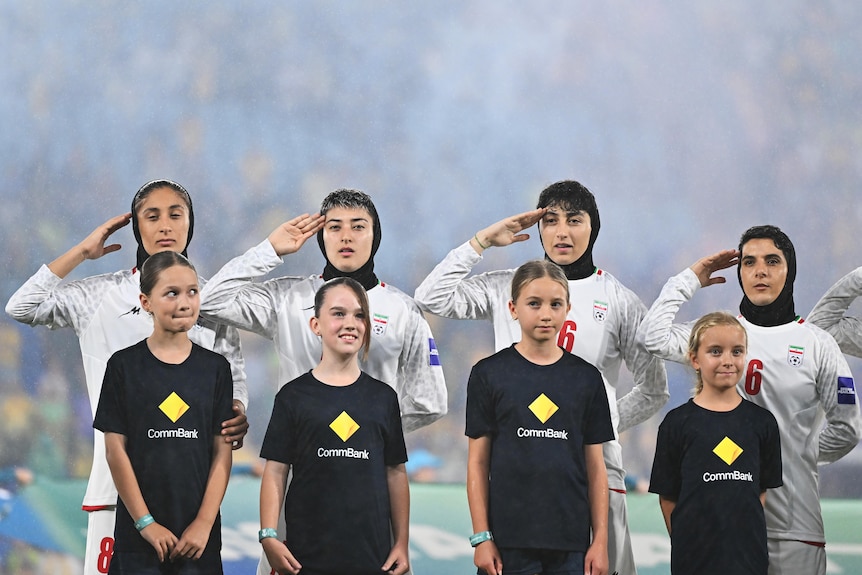 A team of female soccer players and ball girls line up on a pitch