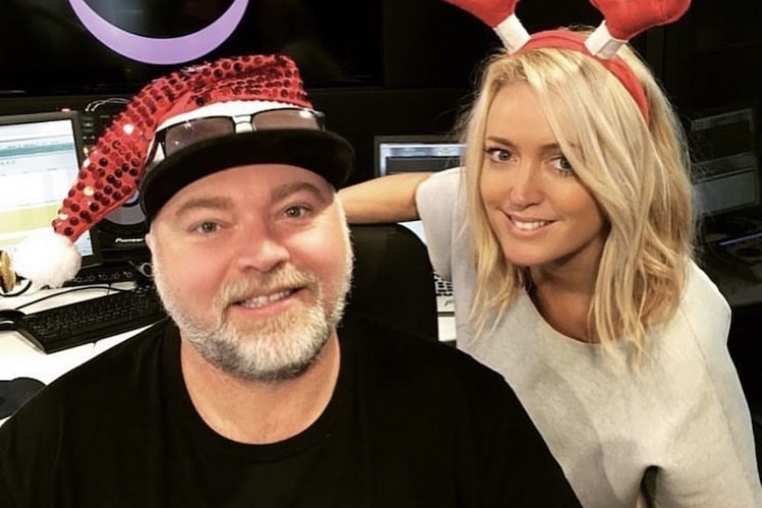 Man seated in black shirt smiling with woman in white leanbing down behind him smiling