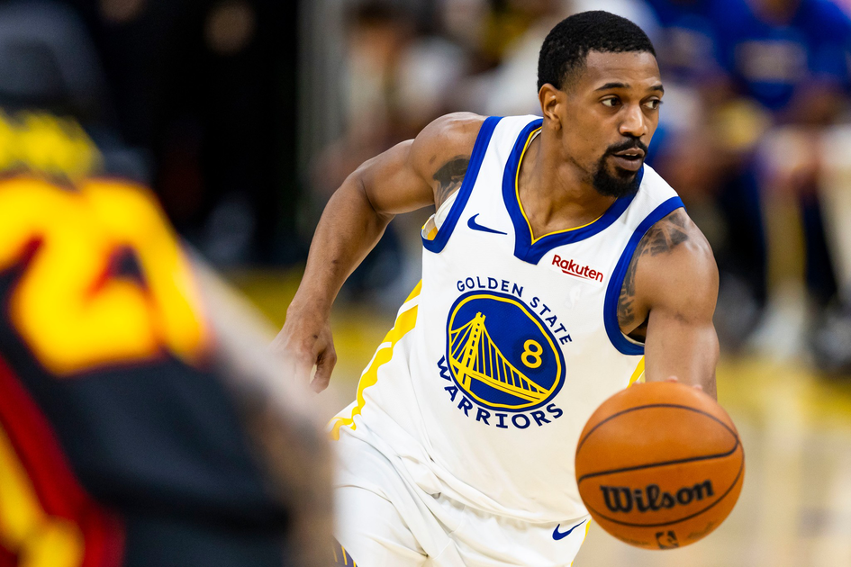 A basketball player in a Golden State Warriors jersey dribbles a Wilson basketball, looking intently to his right during a game.