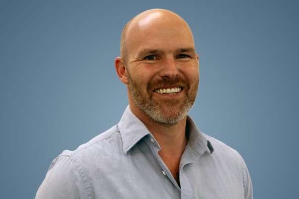 A man wearing a grey shirt in front of a blue background