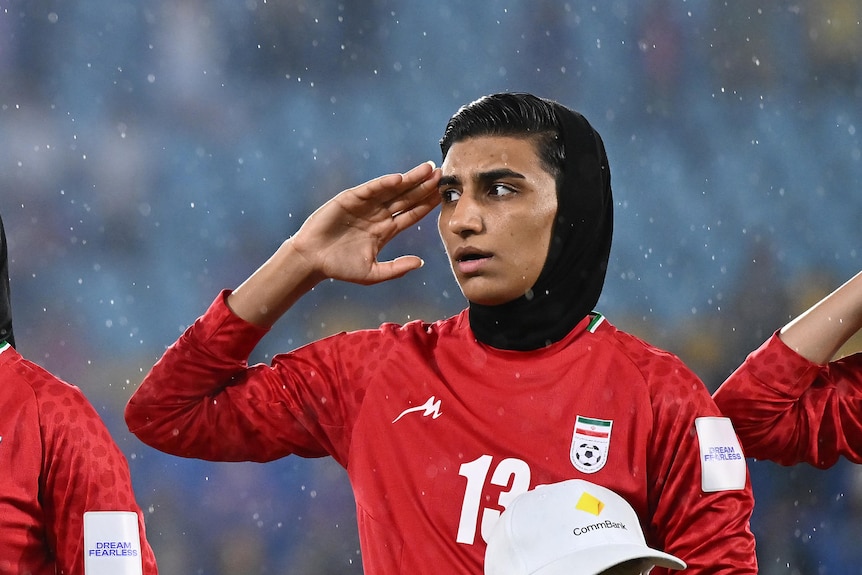 Players from the Iran women's football team salute and sing the national anthem before a game