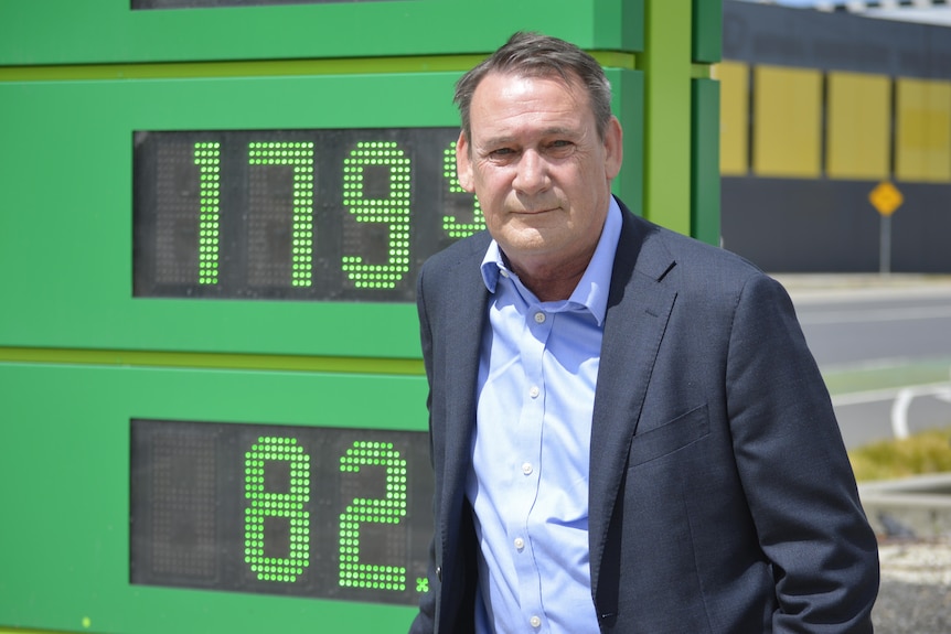 A man standing in front of a price sign at a fuel station.