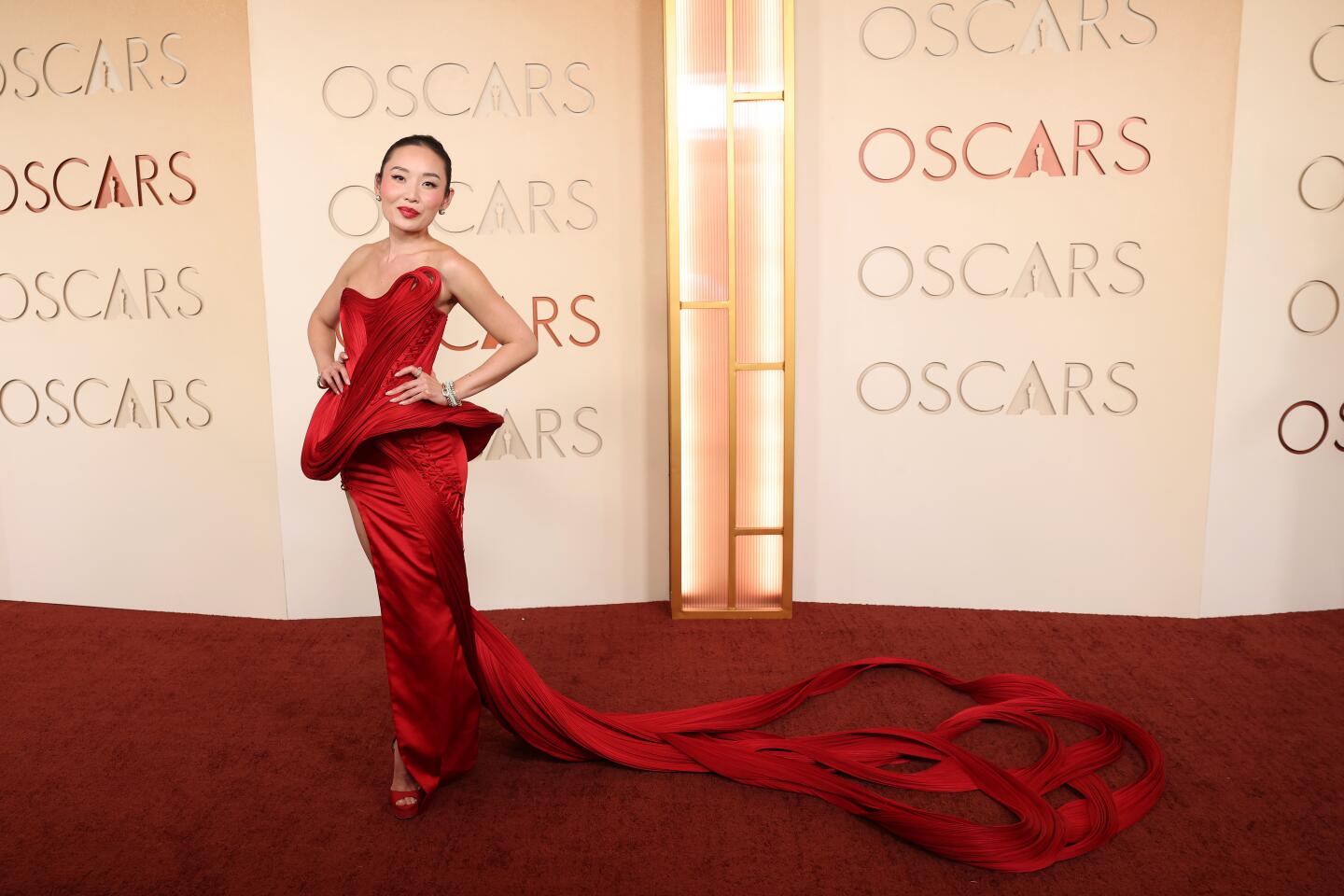 Li Jun Li wearing a red gown with a high slit and a long train, poses on the red carpet.