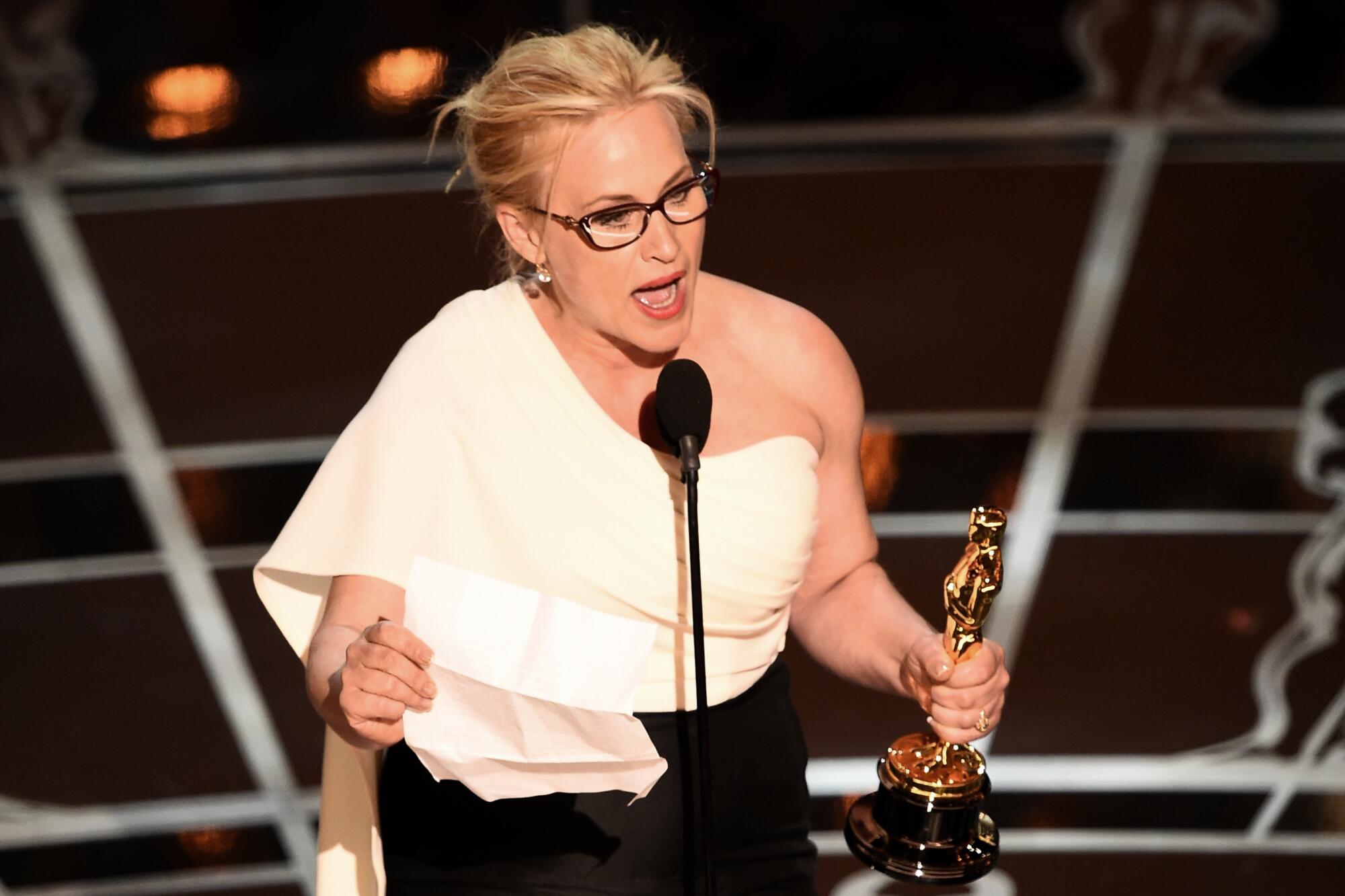 Patricia Arquette talks into a microphone as she accepts her Oscar on stage.