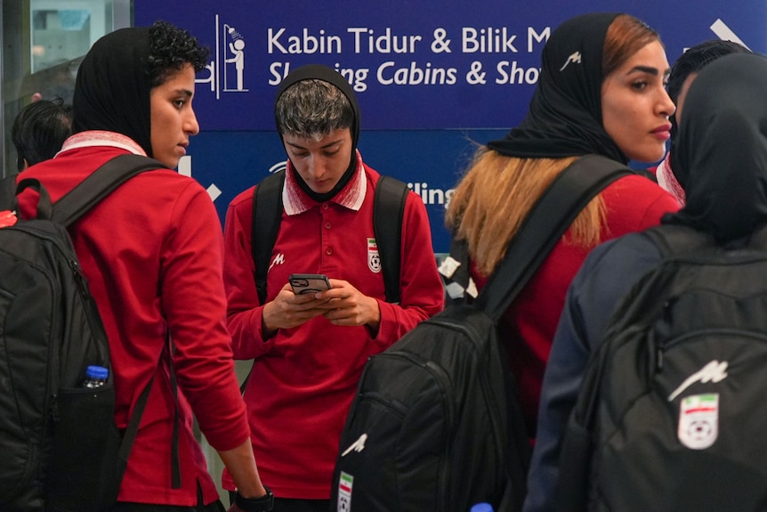 A woman checks her phone, she is surrounded by other women.