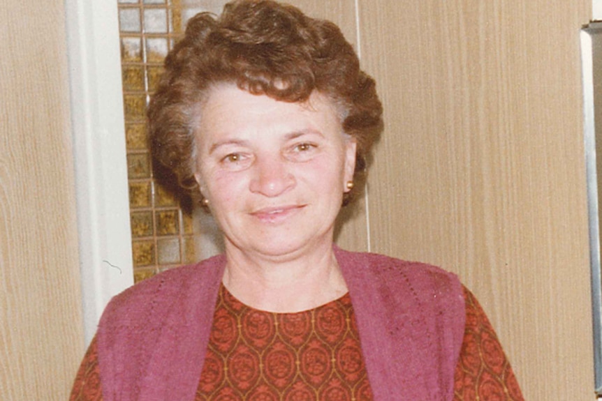 Irma Palasics smiles at the camera, she has short curly hair and wears a pink knit vest.
