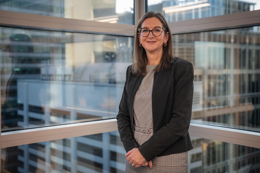 Clare Savage stands by an office window, overlooking other office towers