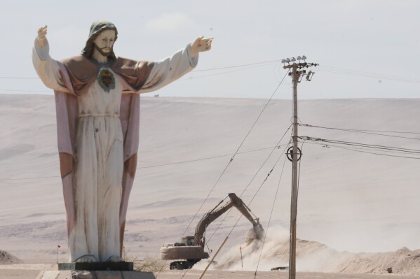 A statue of "Cristo de la Paz" stands on the border crossing between Chile and Peru, as an excavator digs up dirt to install barriers to deter irregular migration, in Chacalluta, Arica province, Chile, Tuesday, March 17, 2026. (AP Photo/Esteban Felix)