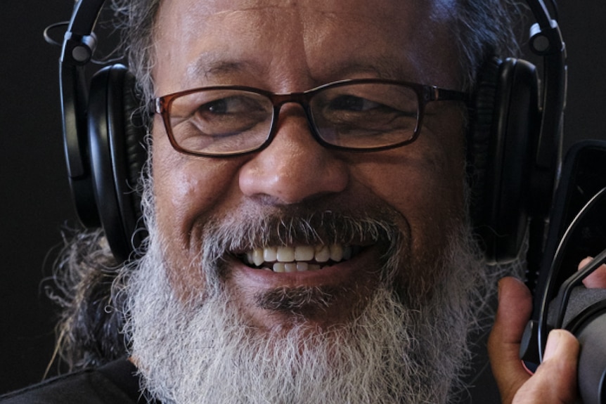 A close-up shot of a bearded middle-aged man speaking into a radio microphone. 