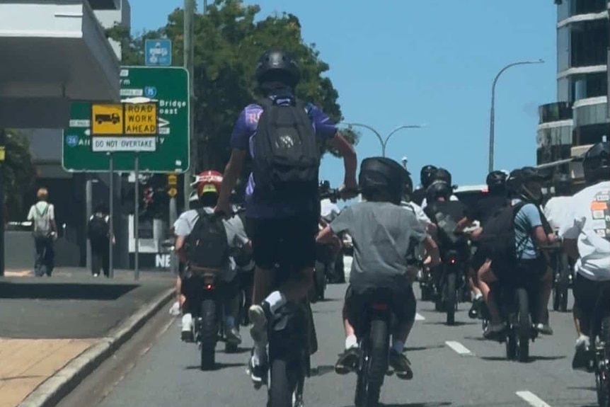 A group of children riding e-bikes on a road pictured from behind.