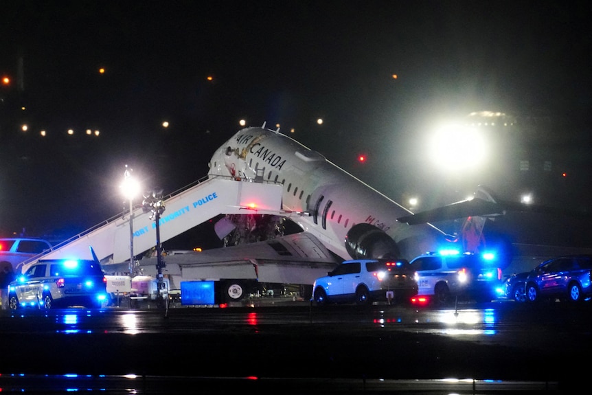 A plane wreck with flashing emergency lights around it
