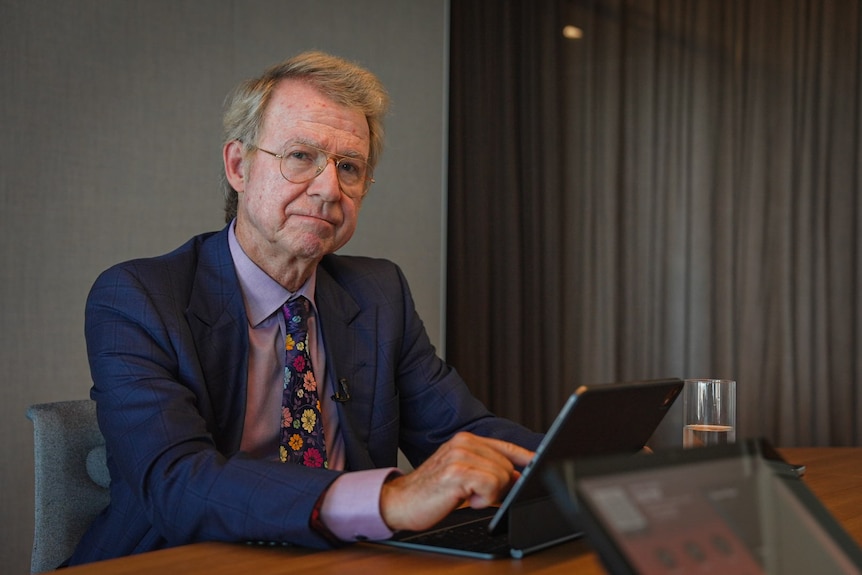 An older man in a suit and tie sitting at a desk with a laptop.
