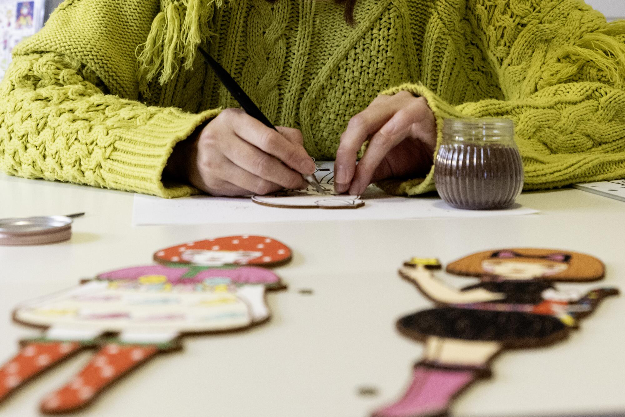 A woman carefully applies sand to a cutout of a cute character.