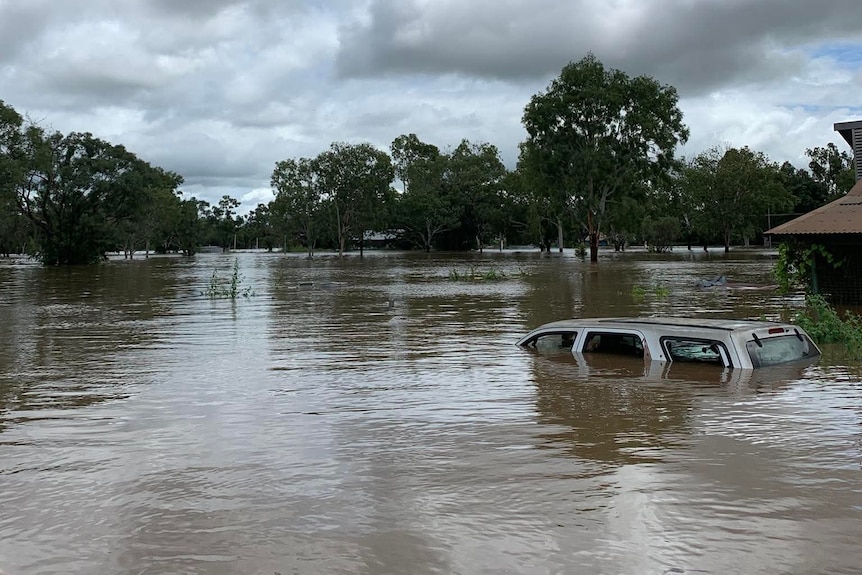 Floodwaters over a remote landscape, including a car that is mostly submerged underwater.