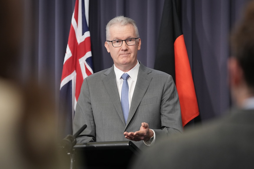 A man in a suit speaks at a lectern.
