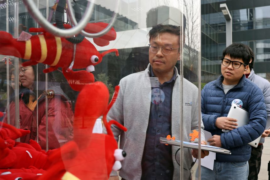 A participant plays a claw machine filled with lobster-shaped plush toys during a setup session for OpenClaw outside the Baidu offices in Beijing.
