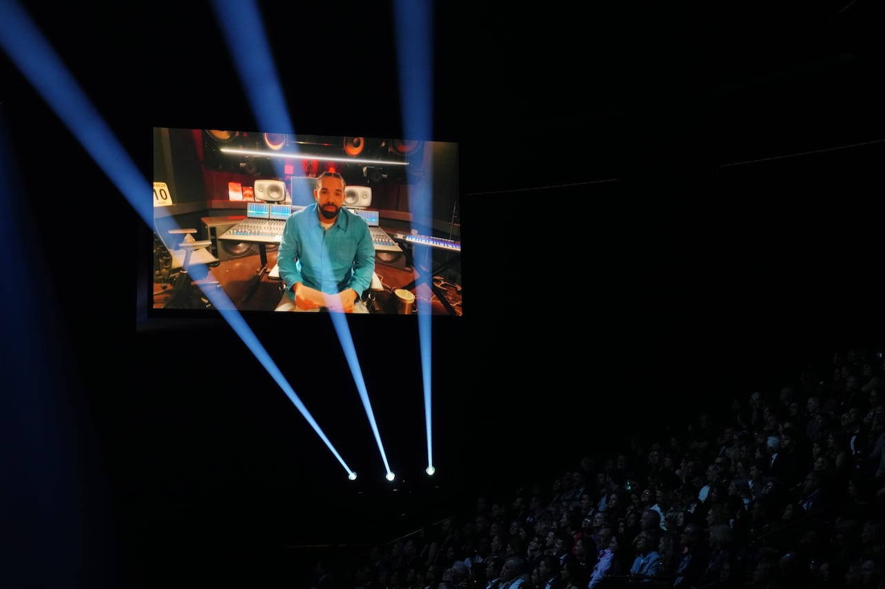 A man on a screen is seen above a crowd in darkness.