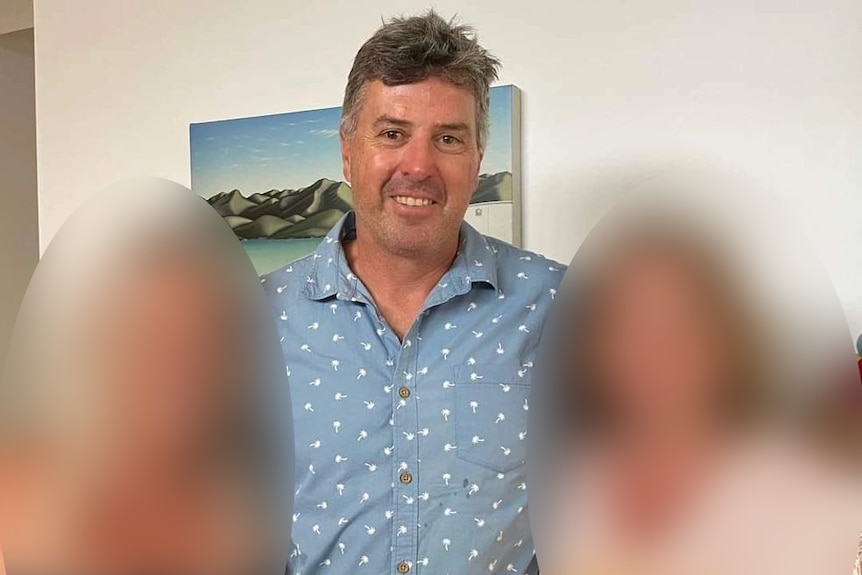 A man stands with two other people who are blurred out.