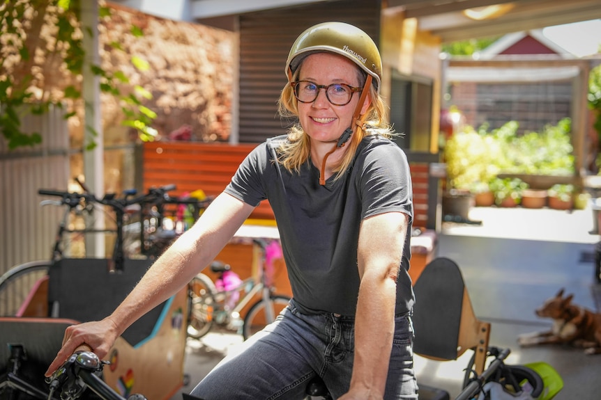 A woman wearing glasses and a helmet on a bicycle in backyard with deck chairs