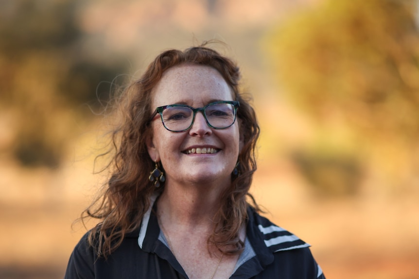 A woman wearing glasses smiling at the camera, taken in an outdoor environment