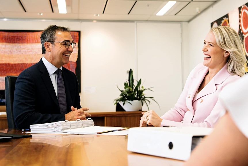 A man and a woman in suits laughing while at a table with folders
