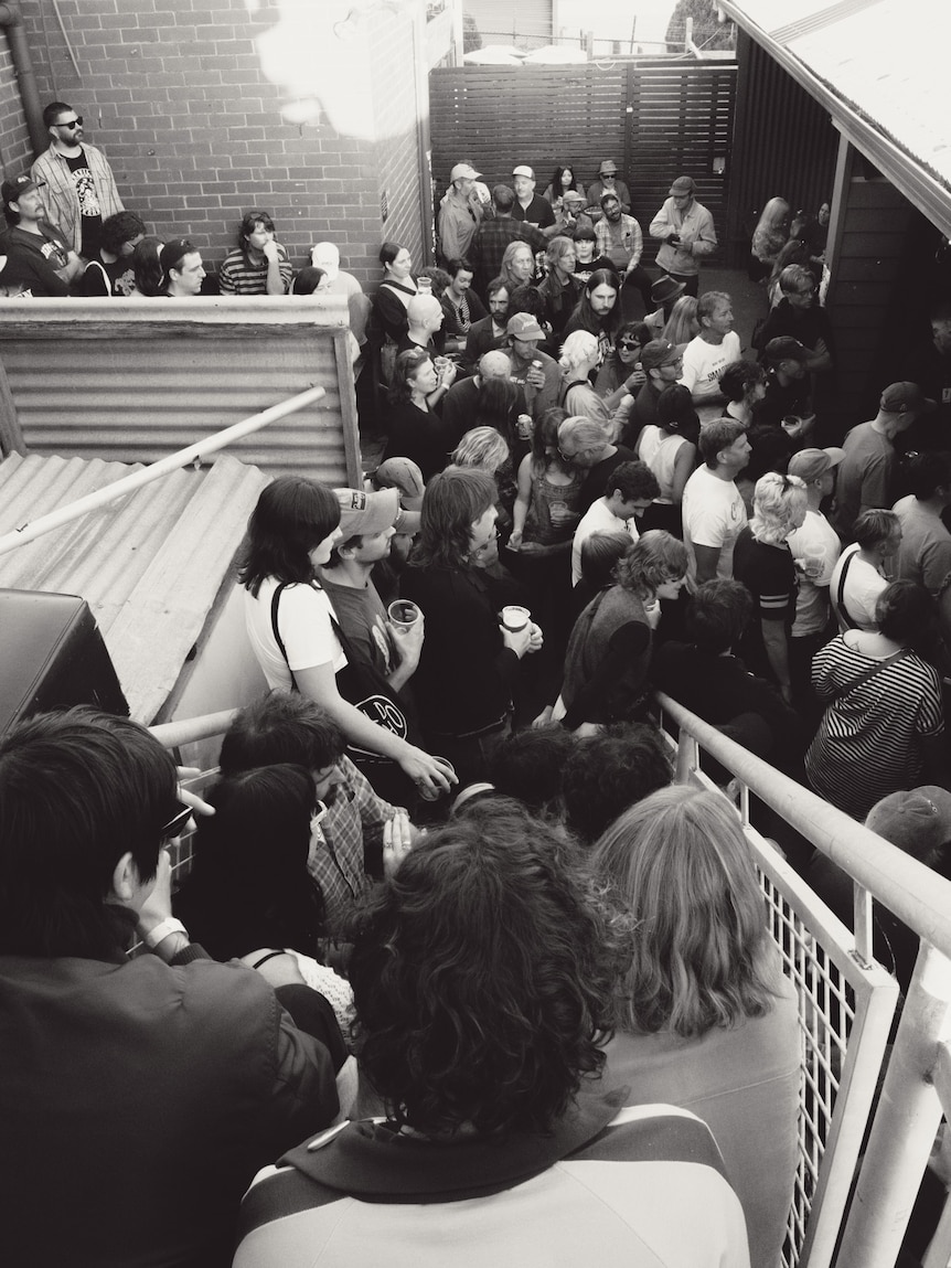 Black and white photo of lots of younger people sitting on an outdoor staircase and gathering near a music stage