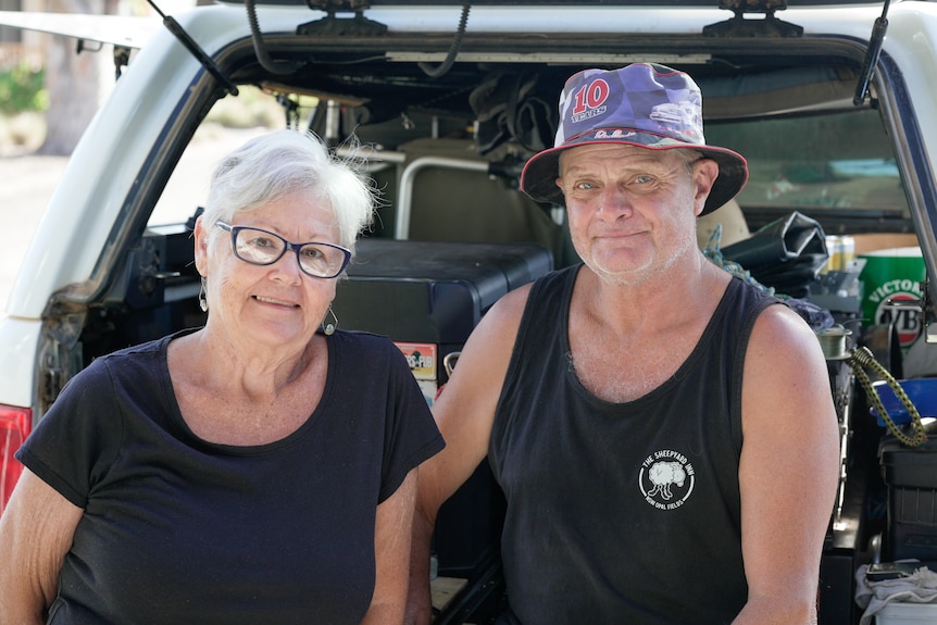 Two older people standing in front of a car.
