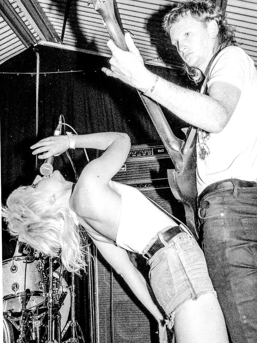 Black and white photo of woman singing bending backwards next to male guitarist
