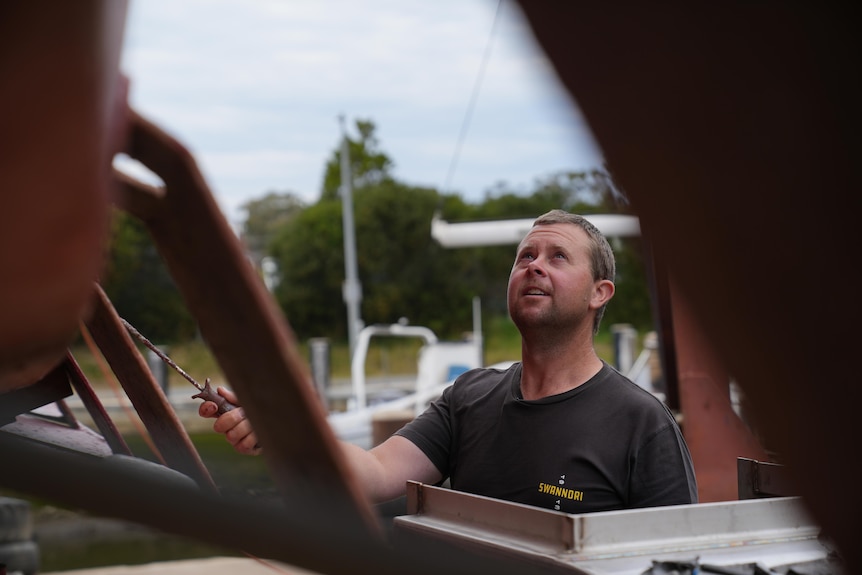 He looks up towards the sky while standing beside his boat, painting it