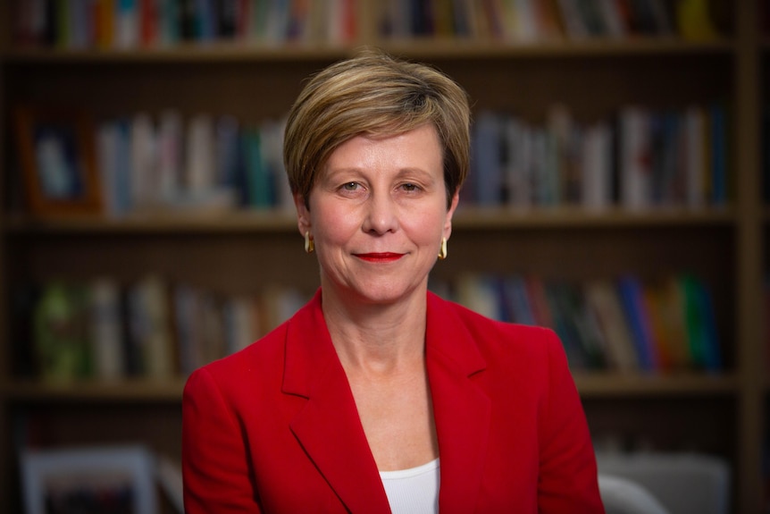 A middle aged white woman with short fair hair and red suit sitting in an office chair