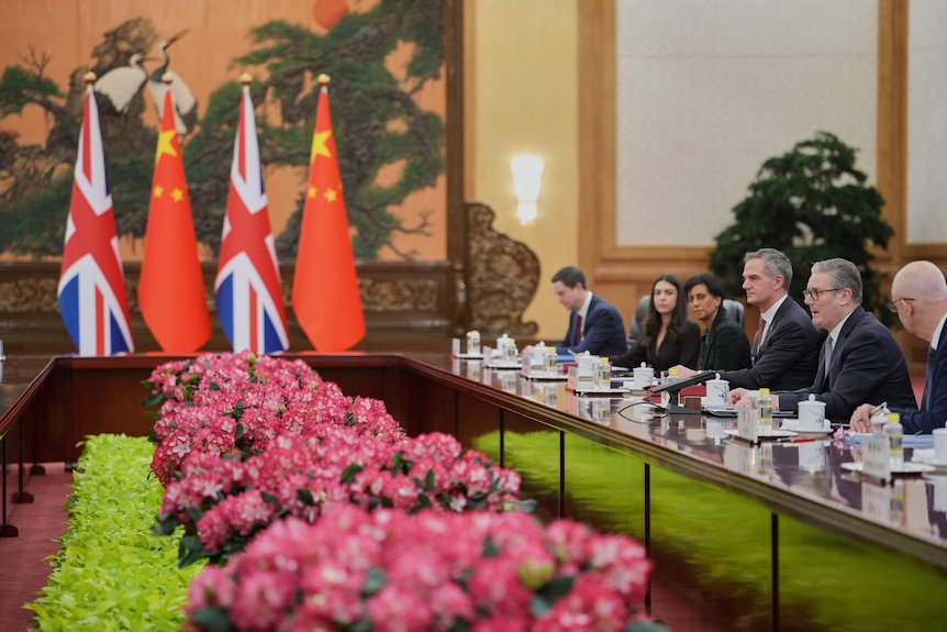 Government officials sit in a row along a long table, with Chinese and UK flags in the centre.