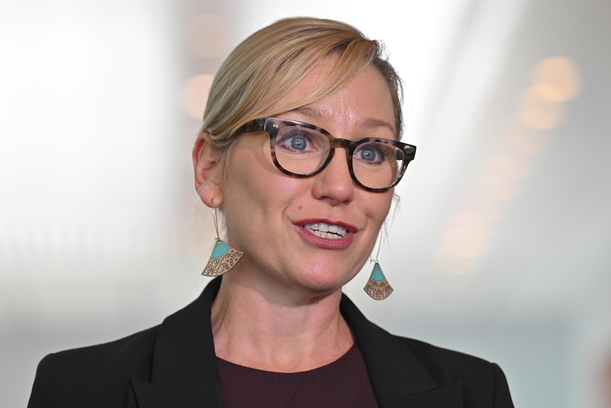 A blonde haired woman wearing glasses speaks