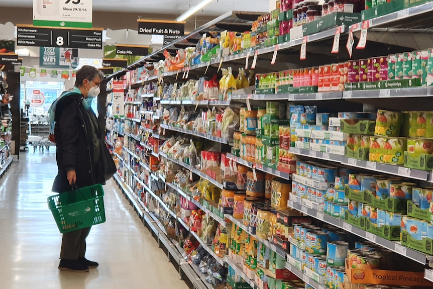 Woman in mask shopping in Woolworths's packaged food aisle.
