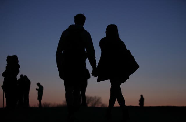 The silhouettes of a couple holding hands at dusk on Parliament Hill, Hampstead Heath, north London