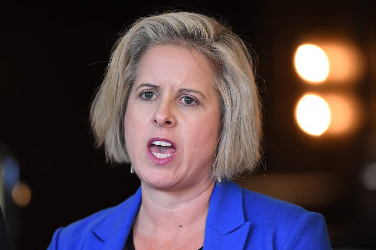 A woman with short blonde hair, wearing a blue blazer.