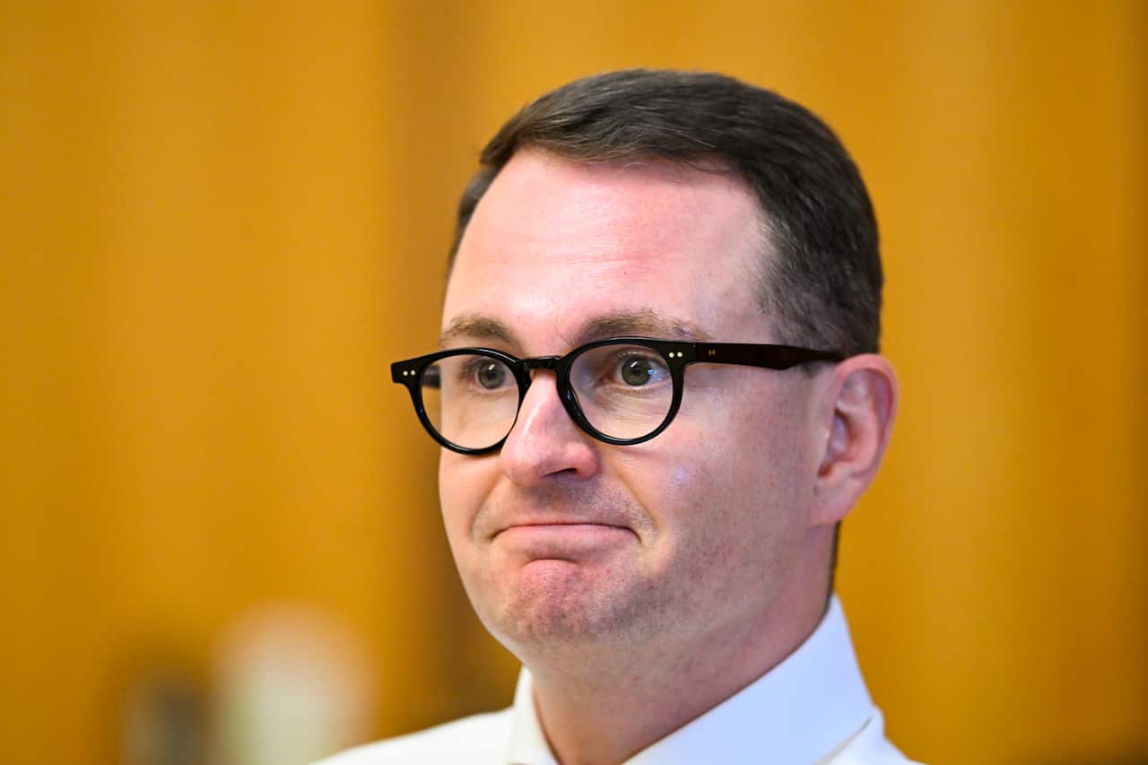 A man wearing a white shirt and glasses is listening while seated.