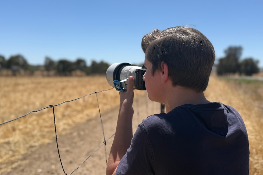 A young man takes a photo on a rural property.