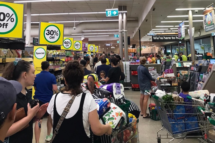 A long line of people in a shopping centre, with full trollies.