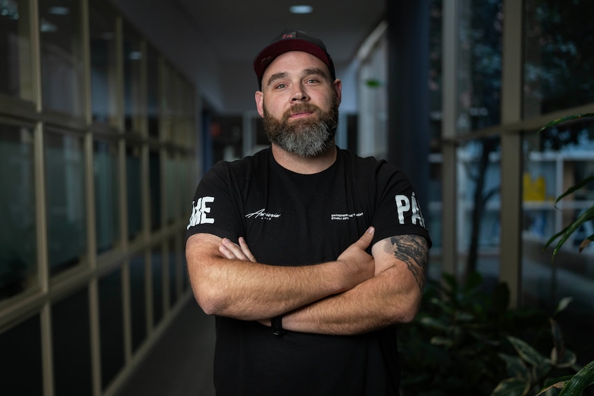 A man in a cap and black t-shirt looking at the camera.