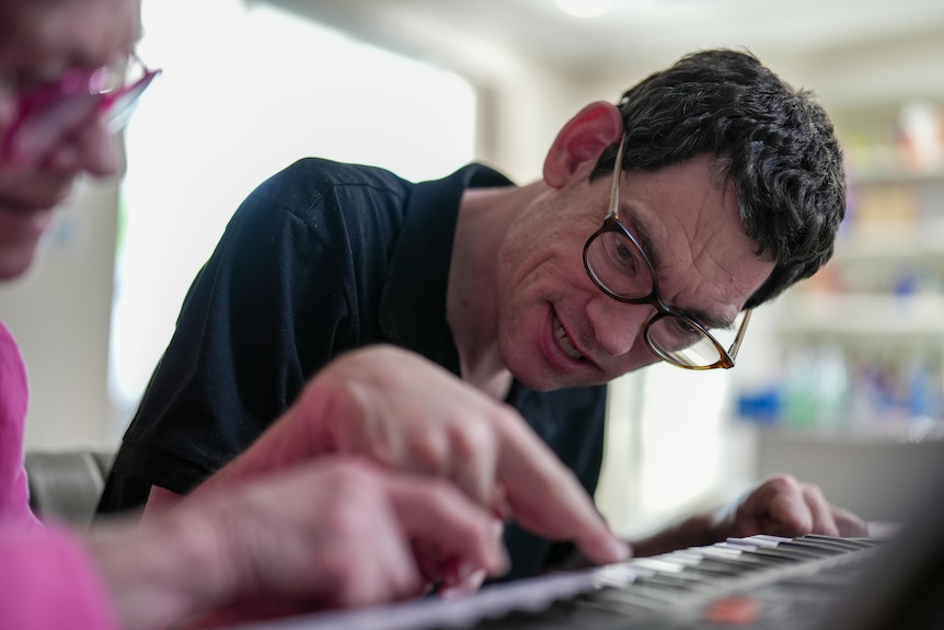 Middle-aged man wearing thick-rimmed glasses leans forward putting his finger on a keyboard key