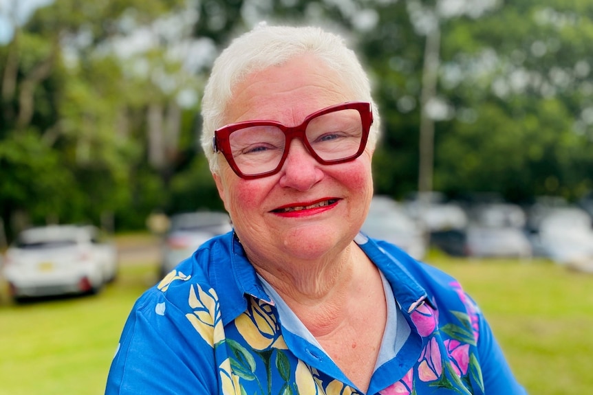A grey haired woman with big red rim glasses is smiling.