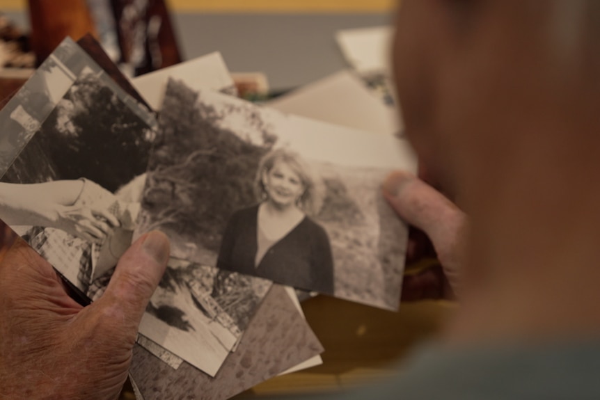 An elderly man's hands, looking over his shoulder, sift through photographs