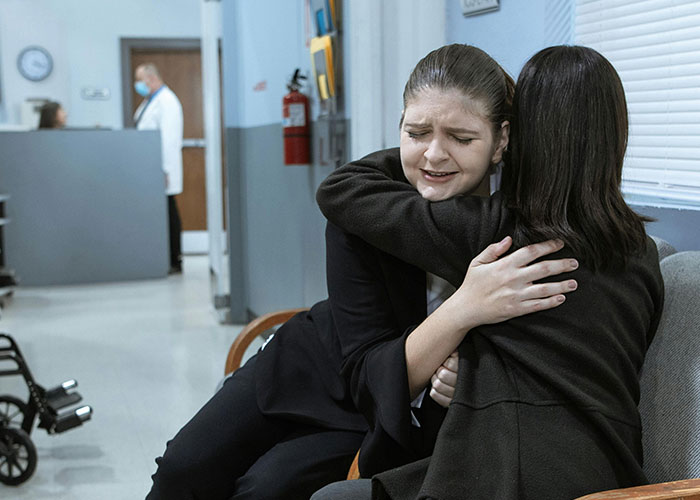 Two women hugging emotionally in a hospital waiting area, illustrating medical secrets and patient fear.