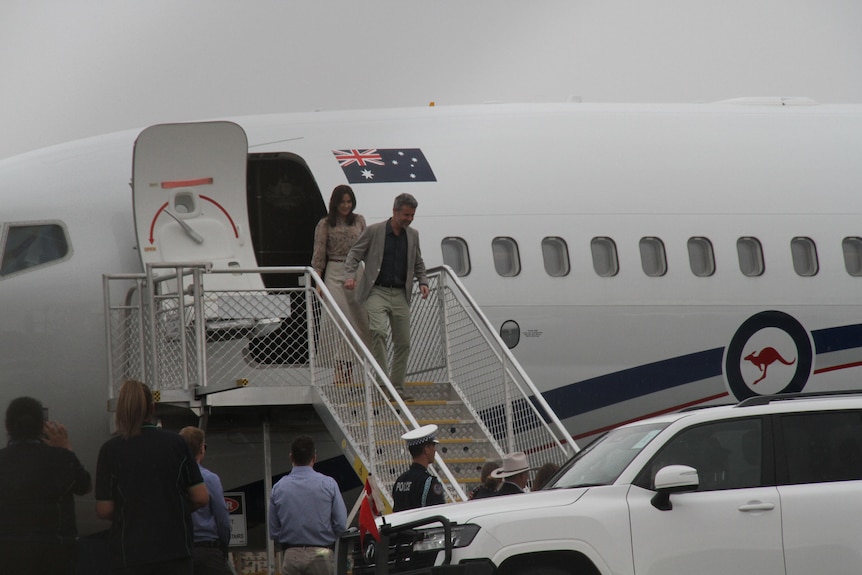 A couple descend a flight of steps from an aeroplane on tarmac.
