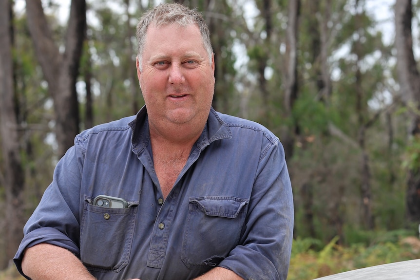 a man leans against a vehicle in front of a bush reserve
